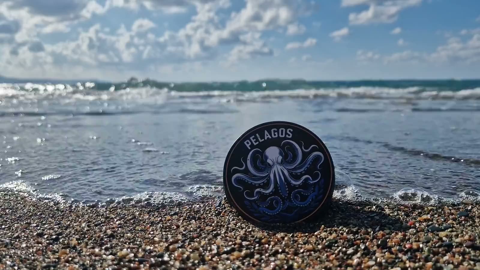 A Pelagos tin of BJJ finger tape on a pebble beach as a wave rolls in